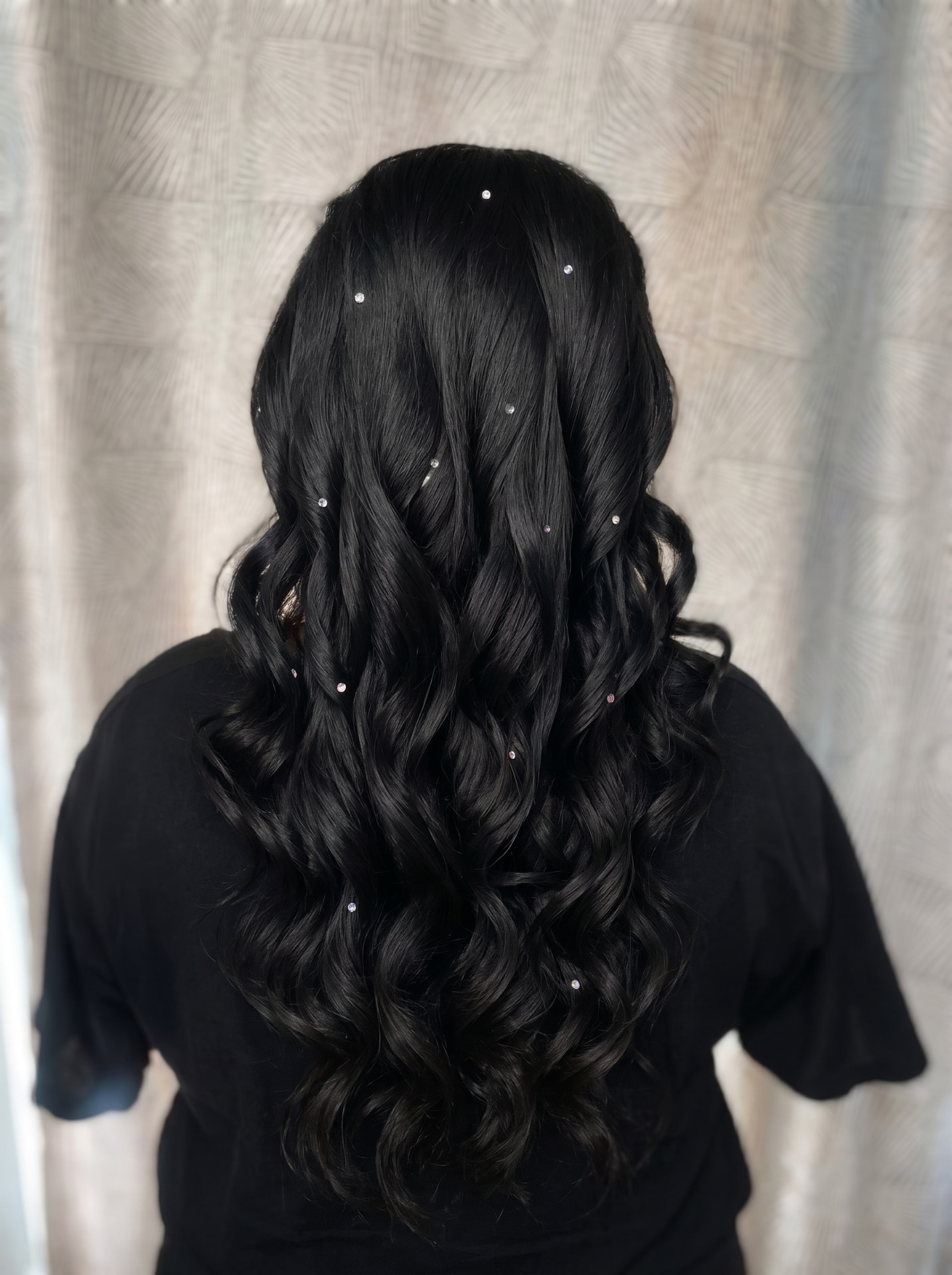 Tatanan rambut panjang gelombang hitam dengan aksesori berkilau dilihat dari belakang