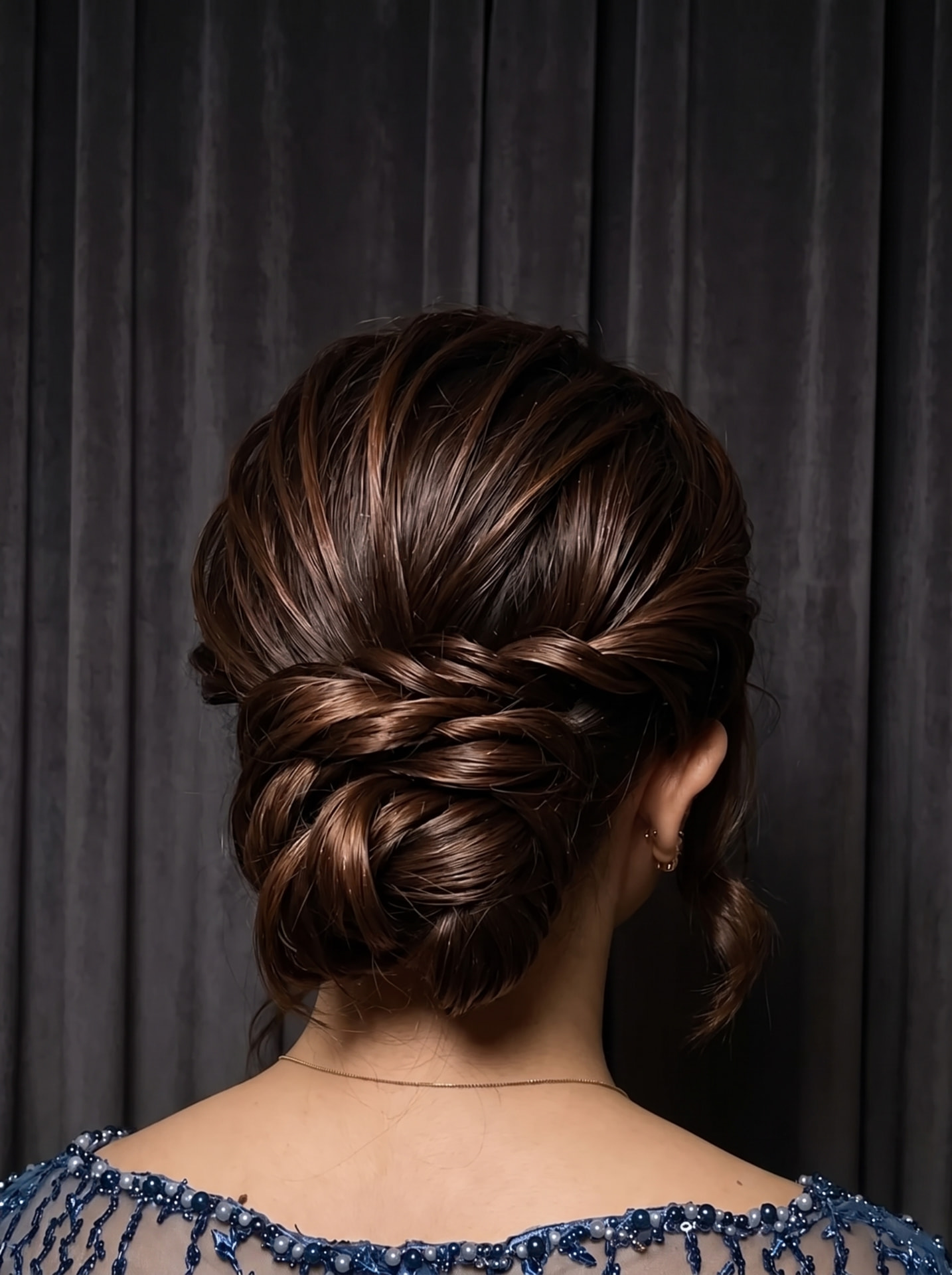 Tatanan low bun bertekstur dengan helai rambut lembut mengurai, dilihat dari belakang
