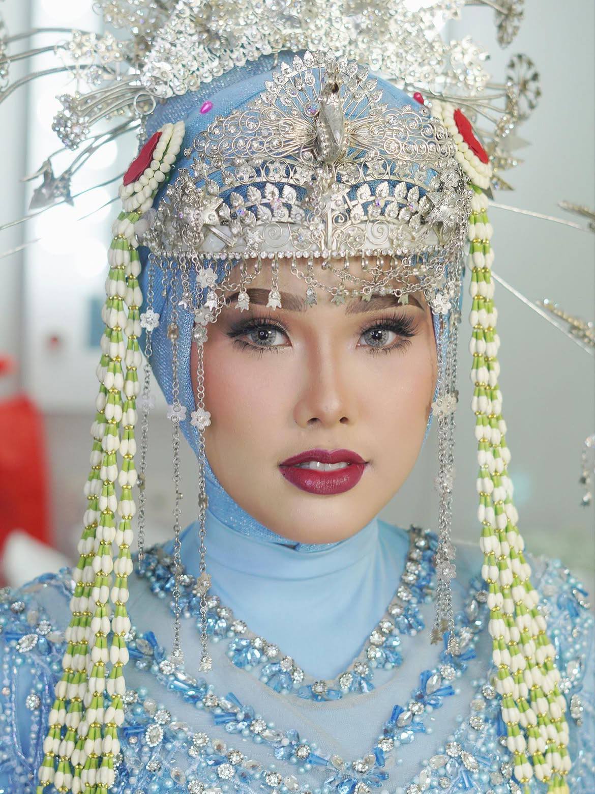 Riasan pengantin tradisional dengan mahkota perak, hiasan kepala, dan busana biru